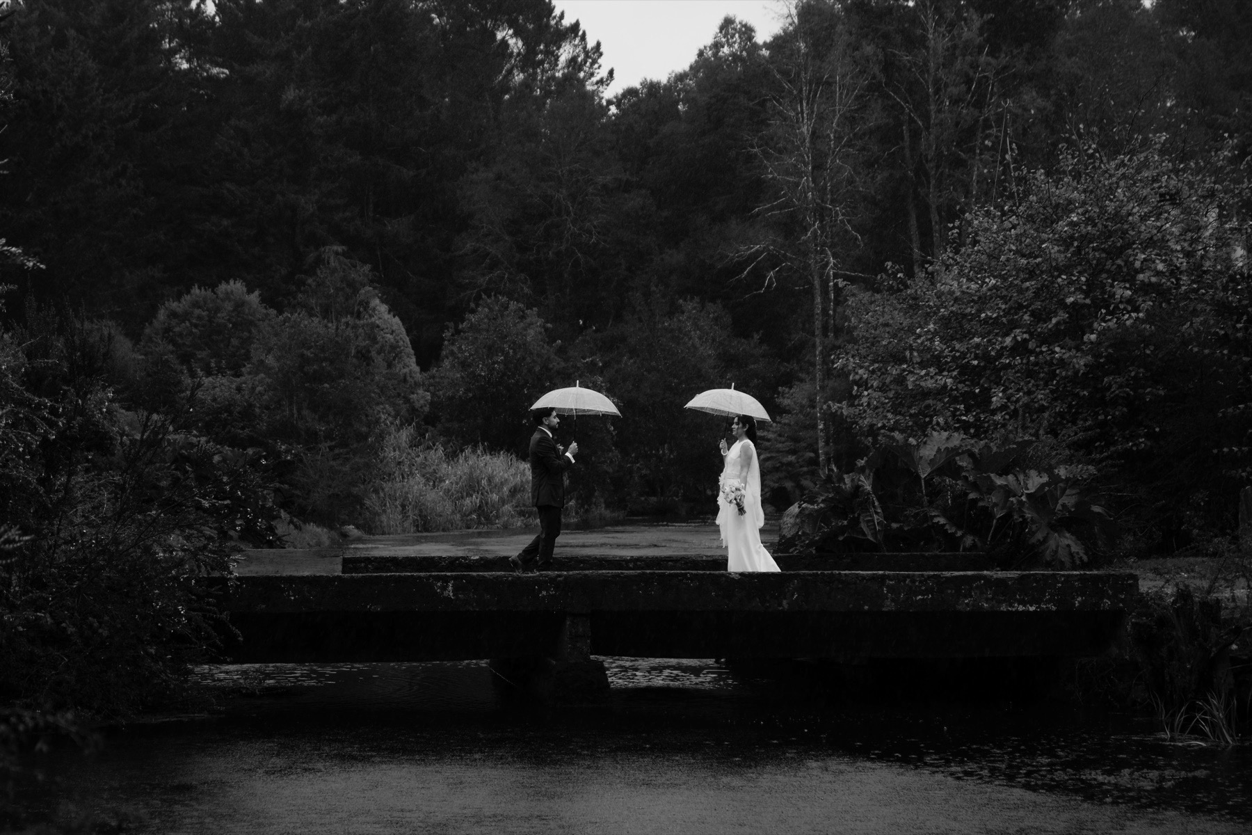 Novios bajo la lluvia en un puente del jardín
